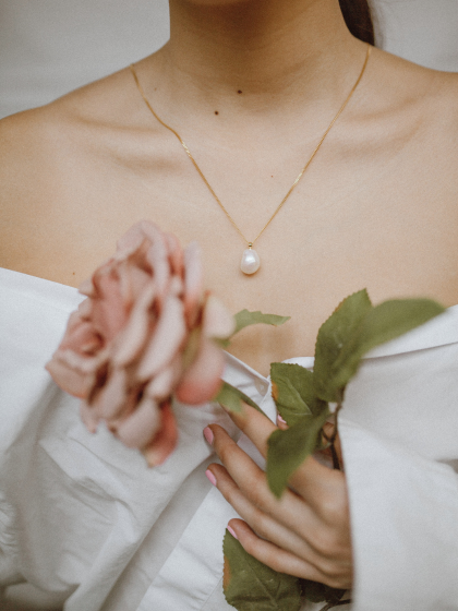 Blick auf das Dekolletee einer Frau mit Perlenhalsband und Rose