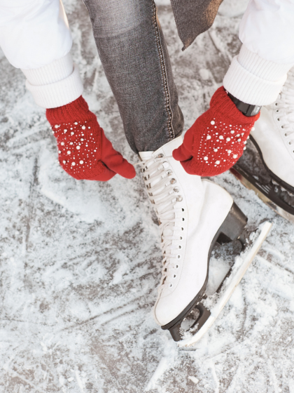 Frau mit roten Handschuhen bindet Eislaufschuhe zu