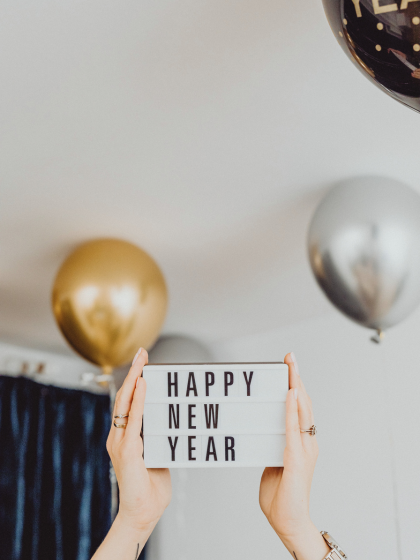 Luftballons & Frauenhände mit Schild "Happy New Year"