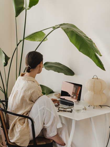 Frau sitzt am Computer in gemütlicher Pose, darüber Pflanze